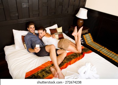 Young couple using a smartphone in a asian hotel room while lying on the bed.  - Powered by Shutterstock