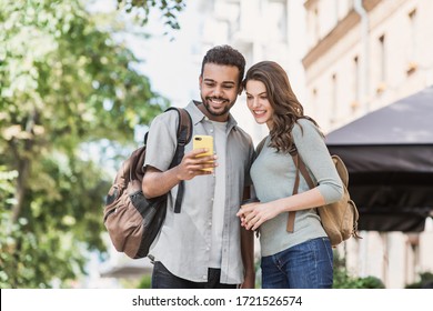 Young couple using smartphone outdoors. Joyful smiling woman and man looking at mobile phone in a city. Relationship, technology, communication, connection, friends, students, summer travel concept - Powered by Shutterstock