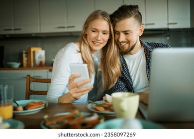 Young couple using a smartphone while having breakfast in the kitchen