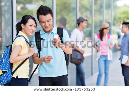 Young couple using smartphone, while their friends talking in the background