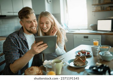 Young couple using the tablet while having breakfast together in the morning in the kitchen at home
