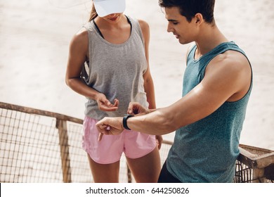 Young Couple Using Wearable Technology During Workout. Young Man Showing Heart Rate Monitor Watch To Woman During Break.