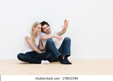 Young couple visualizing the decor of their new home sitting on the bare wooden floor pointing out and discussing placement of furniture