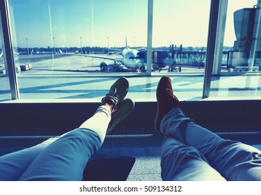 Young Couple Waiting For The Plane At An Airport. Humans Legs With The Plane On The Background Travel Concept  Vintage Colored Picture