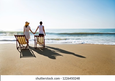 Young couple walk towards the ocean holding hands.