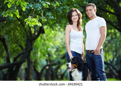 Young Couple Walking With A Dog In The Park