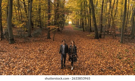 Young couple walking in forest. Elevated view of beautiful woman and handsome man are enjoying scenic autumn fall nature, while talking and holding hands, having a romantic time together.