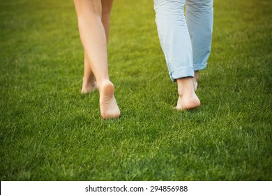 Young Couple Walking On The Grass Without Shoes. Delicate Feet Of Man And Woman In Beautiful Nature.