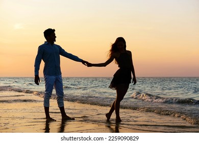Young couple walking at sunset on the beach - Silhouette of lovers holding hands at night by the ocean background - Iconic concept of love and romantic holidays with warm colors at dusk - Image - Powered by Shutterstock