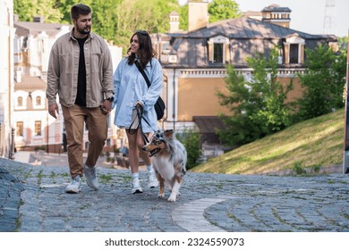 Young couple walking with their aussie shepherd dog in urban area. Happy man and woman walk their pet in the city, real lifestyle