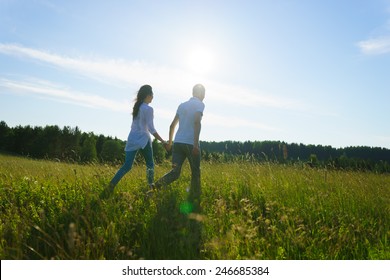 Young Couple Walking Through Green Field