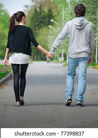 Young Couple Walking Together Hand By Hand  In Park, Rear View