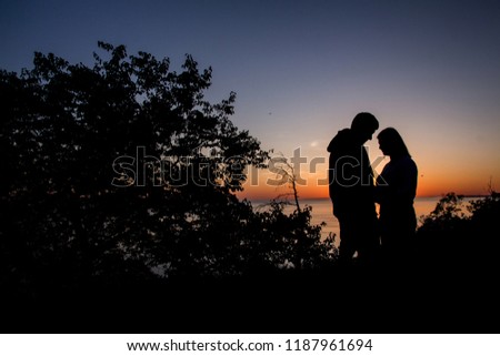 Young couple is walking in the water on summer beach. Sunset over the sea. Two silhouettes against the sun. Just married couple hugging. Romantic love story. Man and woman in holiday honeymoon trip.
