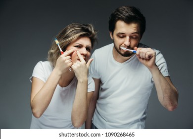 Young Couple Washing. A Man Is Brushing His Teeth, A Girl Has Found A Pimple On Her Face. They Are Tired And Have Not Had Enough Sleep.
