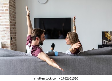 Young couple watch tv with raised hands celebrate win sitting on couch