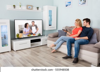 Young Couple Watching Cooking Show On Television At Home