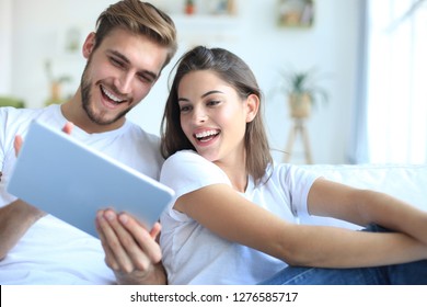 Young couple watching media content online in a tablet sitting on a sofa in the living room. - Powered by Shutterstock