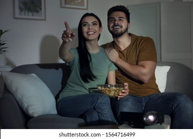 Young Couple Watching Movie Using Video Projector At Home