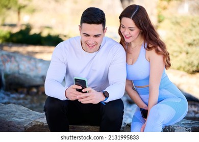 Young Couple Watching Online Content On A Smartphone Sitting In A Park