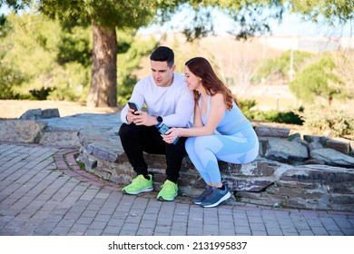 Young Couple Watching Online Content On A Smartphone Sitting In A Park