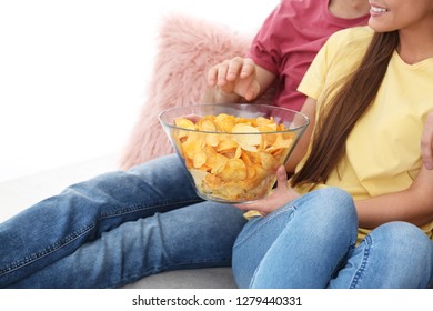 Young Couple Watching TV With Potato Chips On Sofa At Home