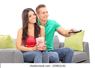 Young Couple Watching TV Seated On A Sofa Isolated On White Background