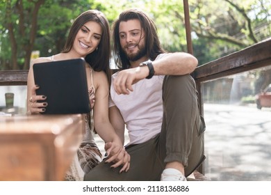 Young Couple Watching Video On Tablet And Holding Hand In Table Outside