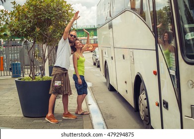 Young Couple Waving Goodbye To Their Friends On The Bus At Bus Station