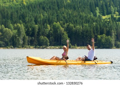 Young Couple Waving And Rowing Kayak On River Summer Vacation