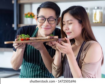 Young couple wearing apron very happy after helping to make a steak at the kitchen in their home,smile and looking the steak on a wooden dish. Couple concept