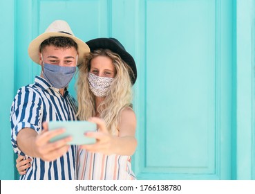 Young couple wearing face mask taking selfie with mobile smartphone on vacation - People having fun traveling again during corona virus outbreak - Love relationship and technology concept 