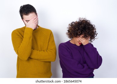 Young couple wearing knitted sweater standing against white background making facepalm gesture while smiling amazed with stupid situation.
