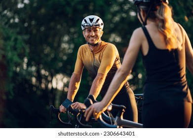 Young couple wearing sportswear and protective helmet taking a break while riding bikes outside of the city. Competition and regular training. Focus on a man wearing cycling gear. Copy space. - Powered by Shutterstock