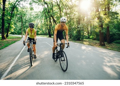 Young couple wearing sportswear and protective helmet while riding bike on a paved road outside of the city. Competition and regular training. Healthy lifestyle concept. Copy space.