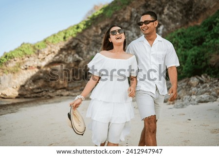 young couple in white laughing and walking at the beach for vacation together