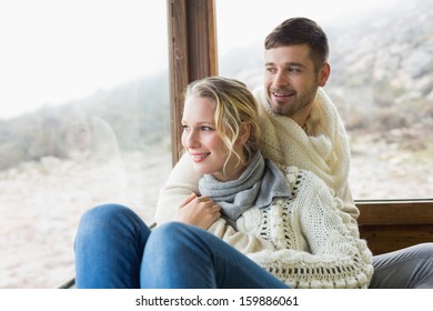 Young Couple In Winter Clothing Looking Out Through Cabin Window