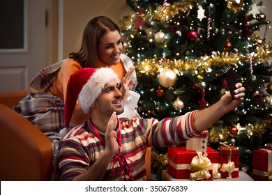 Young Couple Wishing Happy New Year Or Merry Christmas To Someone Using Smart Phone For Video Call