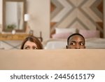 Young couple, woman and man comically hiding behind the sofa, close up