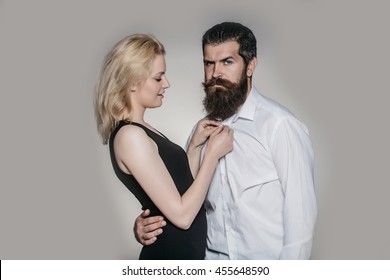 Young Couple Of Woman With Pretty Face And Blonde Hair In Black Vest And Handsome Bearded Man With Long Beard In White Shirt In Studio On Grey Background