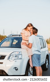 Young Couple Woman Sitting On Car Hood Man Kissing Her. Copy Space