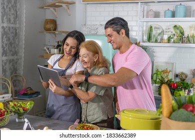 Young Couple Working With Grand Mom To Take Online Cooking Course And Prepare Meal At Home. Happy Family Is Cooking Breakfast With Healthy Organic Food Together