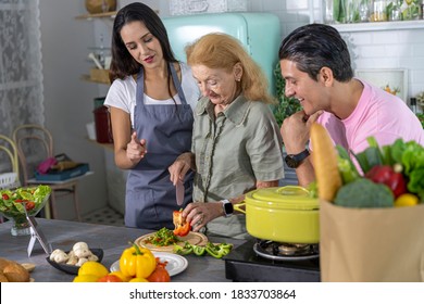 Young Couple Working With Grand Mom To Prepare Meal At Home. Happy Family Is Cooking Breakfast With Healthy Food Together