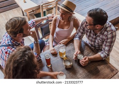 Young couples drinking beer and laughing together at the bar. Happy friends having fun at bar - Young trendy people drinking beer and laughing together. Oktoberfest and St Patrick's day beer festivals