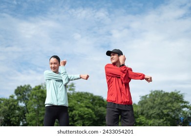 Young couples exercise in blue and red sports clothes. The two of them stood and stretched their upper arms. outdoor exercise Exercise in the stadium maintaining health exercise active living