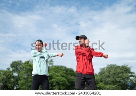 Young couples exercise in blue and red sports clothes. The two of them stood and stretched their upper arms. outdoor exercise Exercise in the stadium maintaining health exercise active living