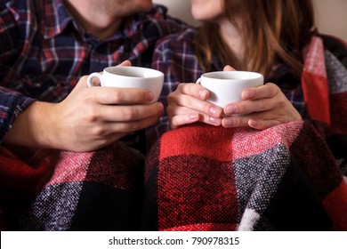 Young couple's hands with two cups of hot coffee. Man and woman together in a warm blanket. - Powered by Shutterstock