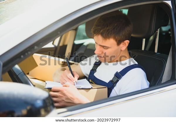 Young\
courier with clipboard and parcels in delivery\
car