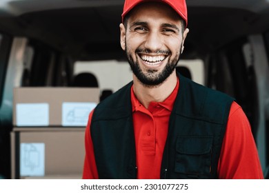 Young courier delivery man smiling into the camera while standing in front of his van transportation - Powered by Shutterstock