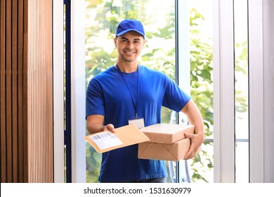 Young Courier Holding Parcels On Doorstep. Delivery Service