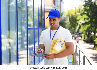 Young courier with padded envelopes and clipboard outdoors. Delivery service